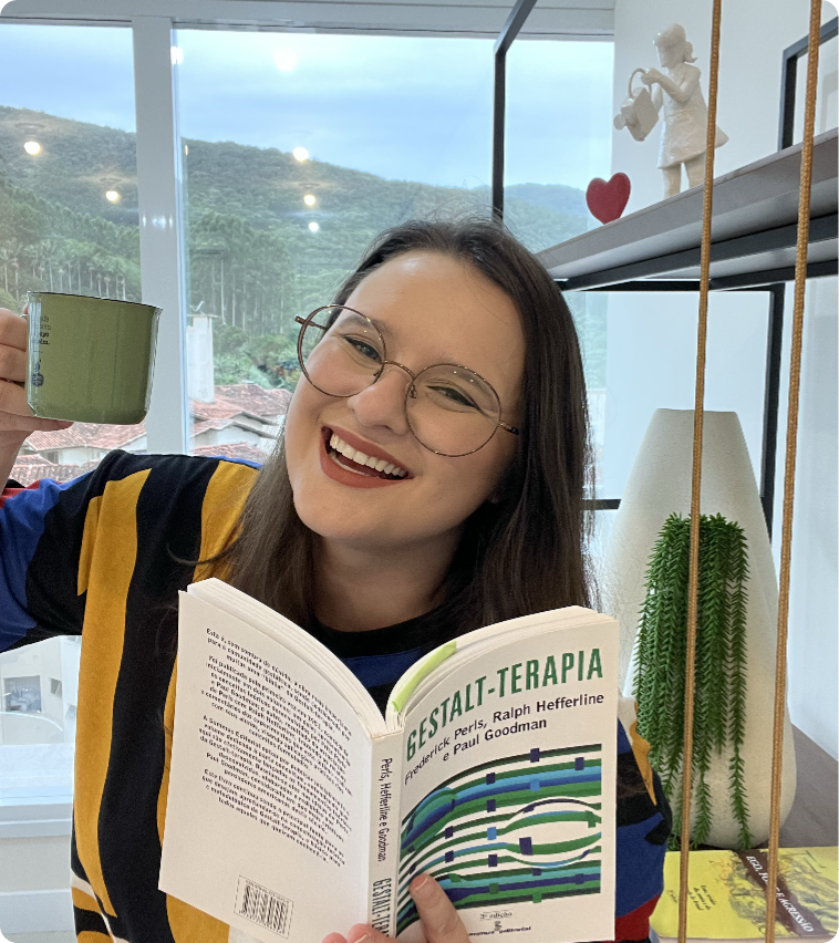 Psicóloga Natália sorrindo com um livro e um café